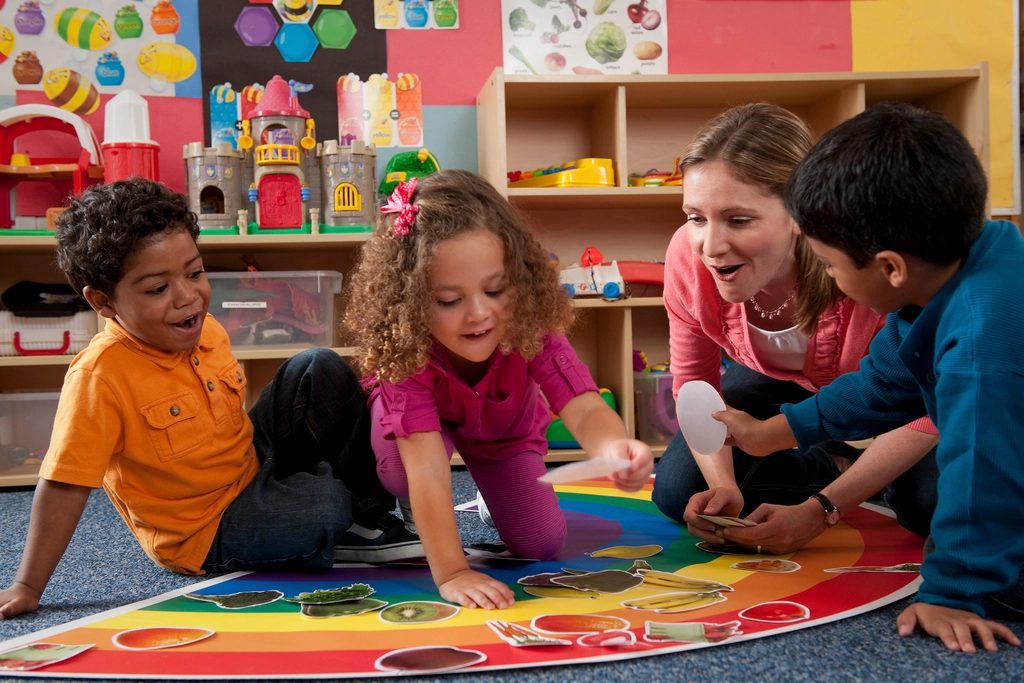 Peuters spelen samen met een pedagogisch medewerker op een kleurrijk speelkleed
